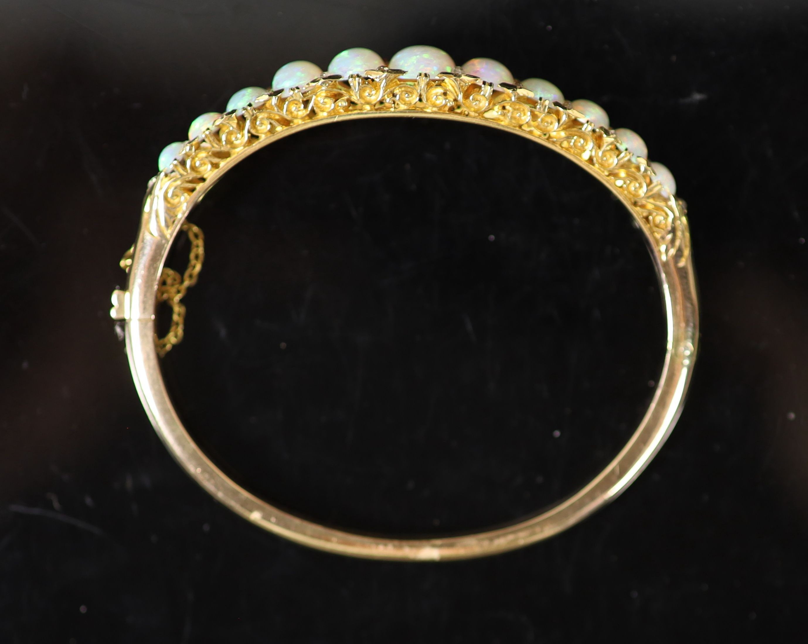 An Edwardian gold and graduated eleven stone white opal set hinged bracelet, with diamond chip spacers